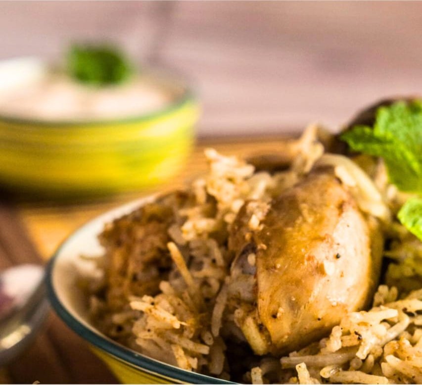 Chicken piece over pulao with mint and a bowl of raita behind